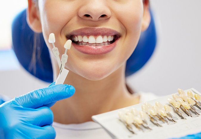 Woman smiling while a dentist holds veneers in front of her teeth